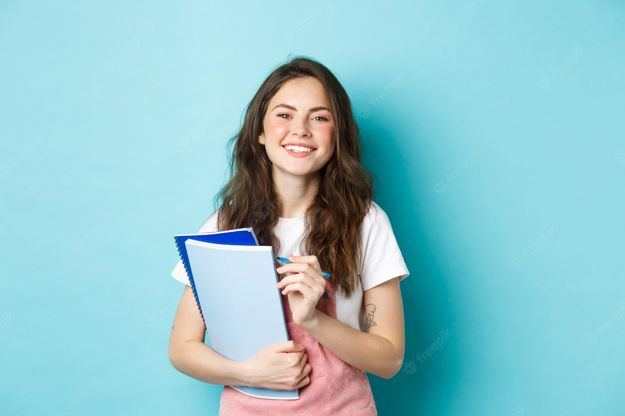 happy-young-female-student-holding-notebooks-from-courses-smiling-camera-standing-spring-clothes-against-blue-background_1258-70161